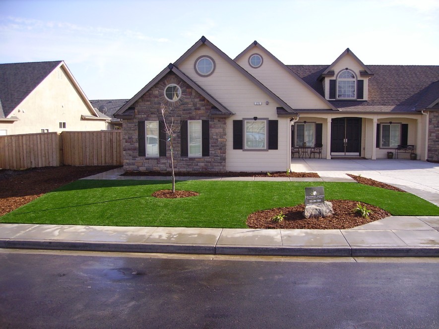 Best artificial lawns installed in a residential front yard with mulch flower beds, a young tree, and stone-accented craftsman home with covered front porch